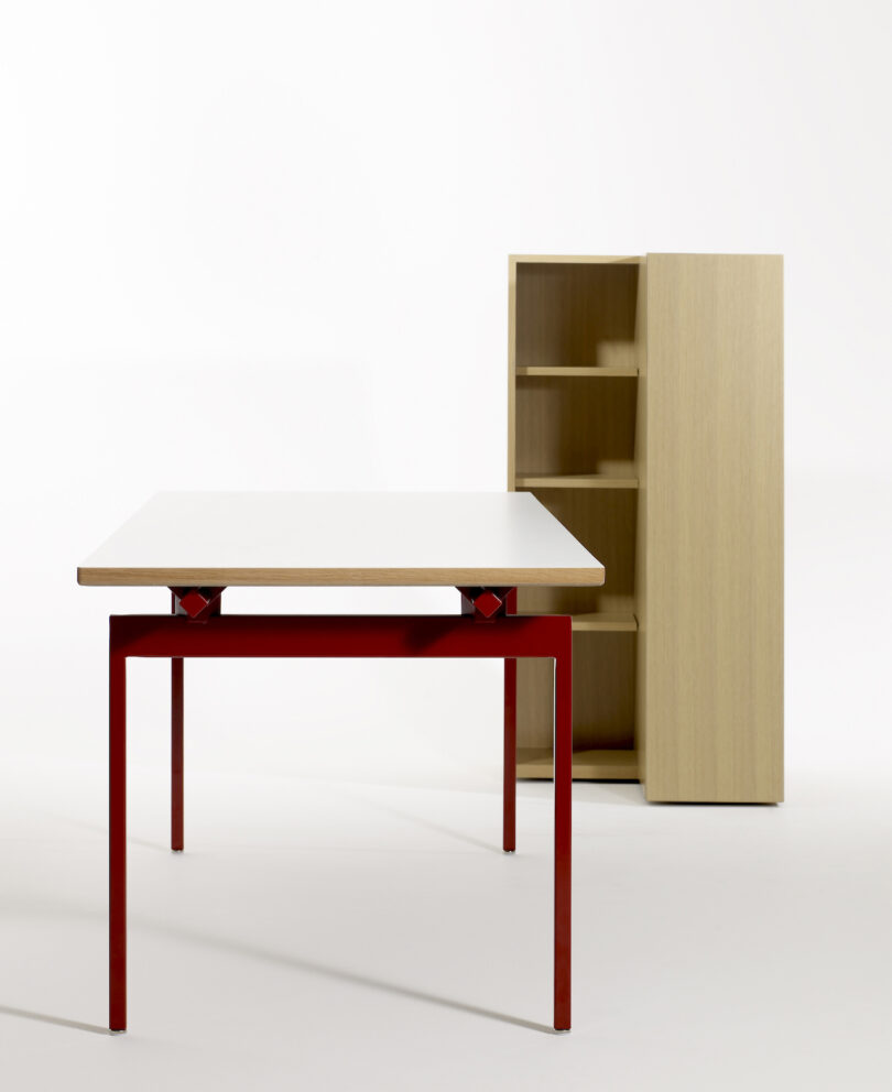 Modern minimalist desk with red metal frame and light wood shelving unit.