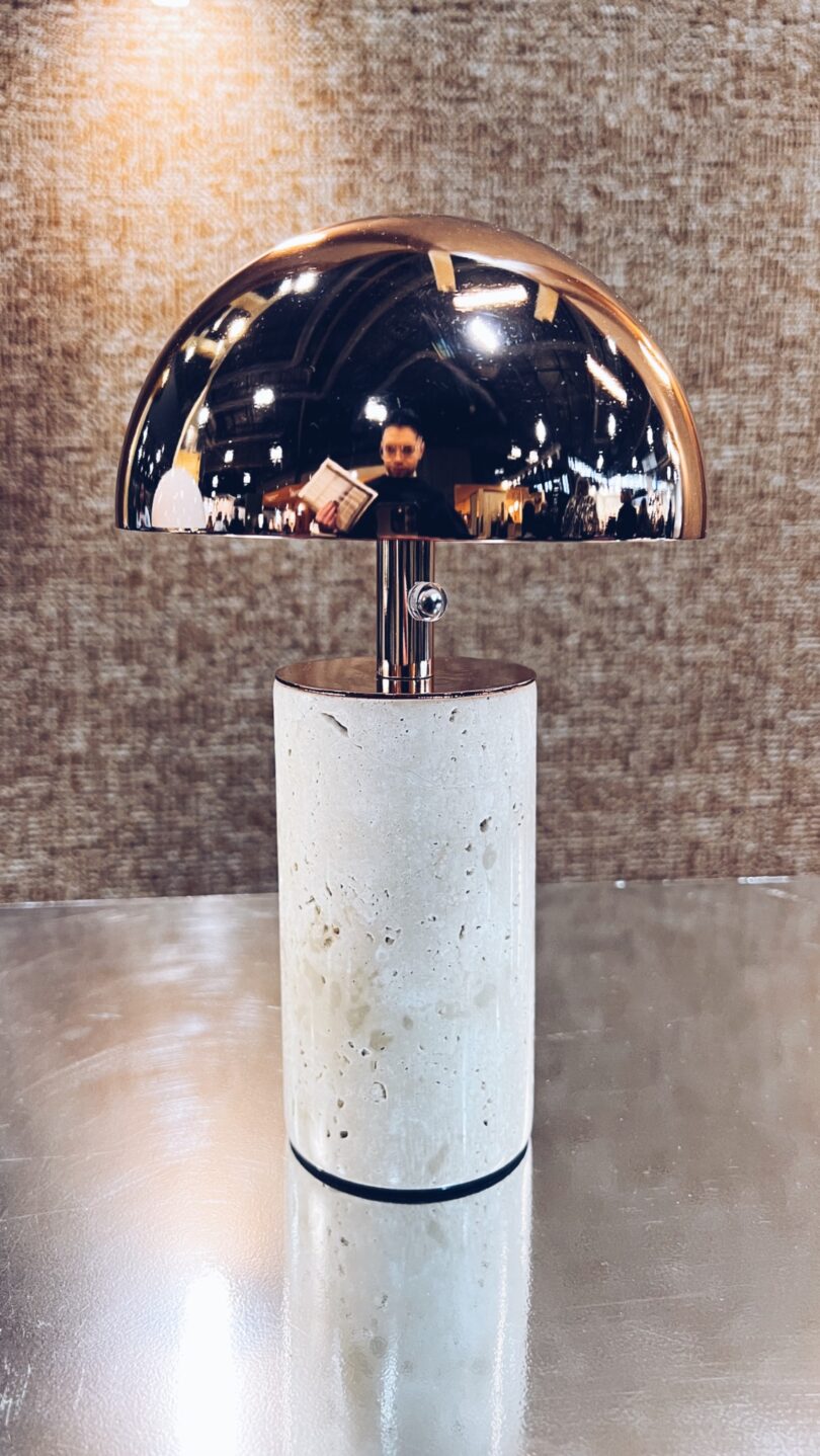 A modern chrome table lamp with a stone base on a reflective surface.