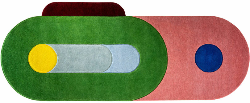 Close-up of a colorful geometric rug by Sam Buckley with overlapping shades of red, pink, and blue.