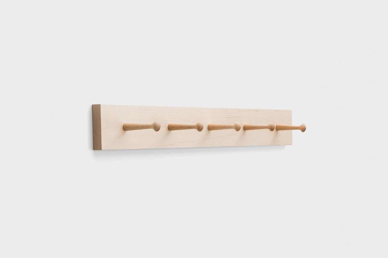 A simple maple peg rail with five pegs mounted on a white wall.