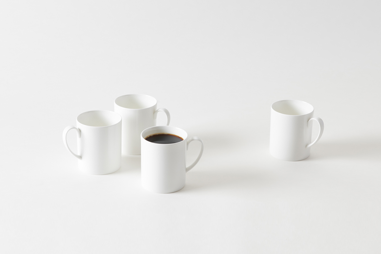 Minimalist white ceramic mugs arranged on a clean surface, one filled with coffee, showcasing modern design against a neutral background.