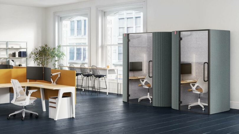 A modern open-plan office with workstations and two soundproof pods situated near windows.