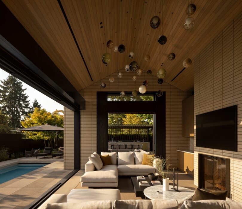 Indoor-outdoor living room with a vaulted wood ceiling and views of a patio and swimming pool.