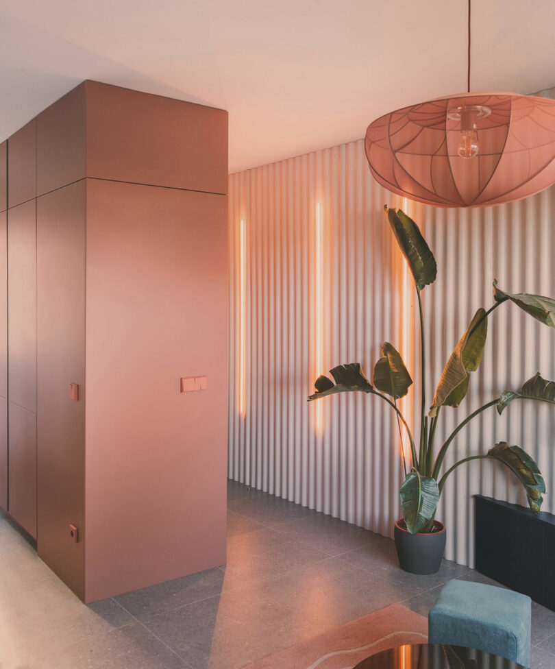 Hallway with pink built-in cabinets and ribbed beige wall paneling with vertical orange light fixtures.