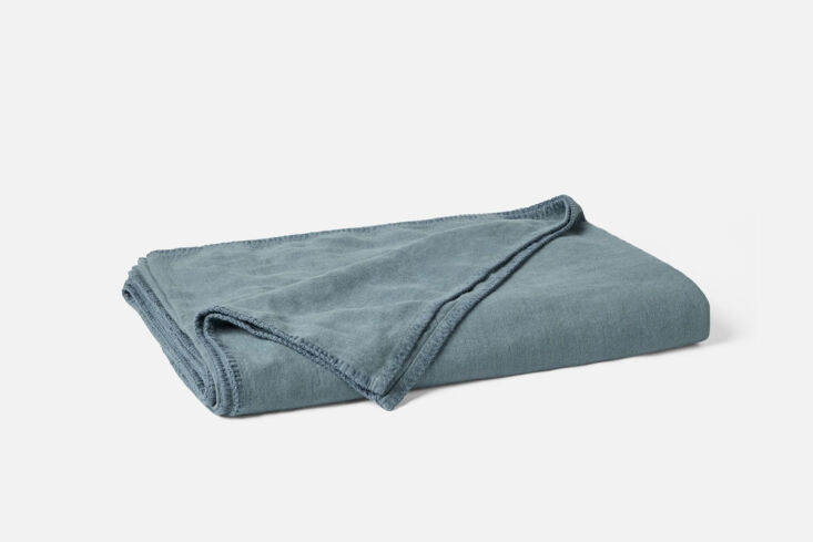 A blue-toned Helena Organic Linen Blanket from Coyuchi draped over a bed.