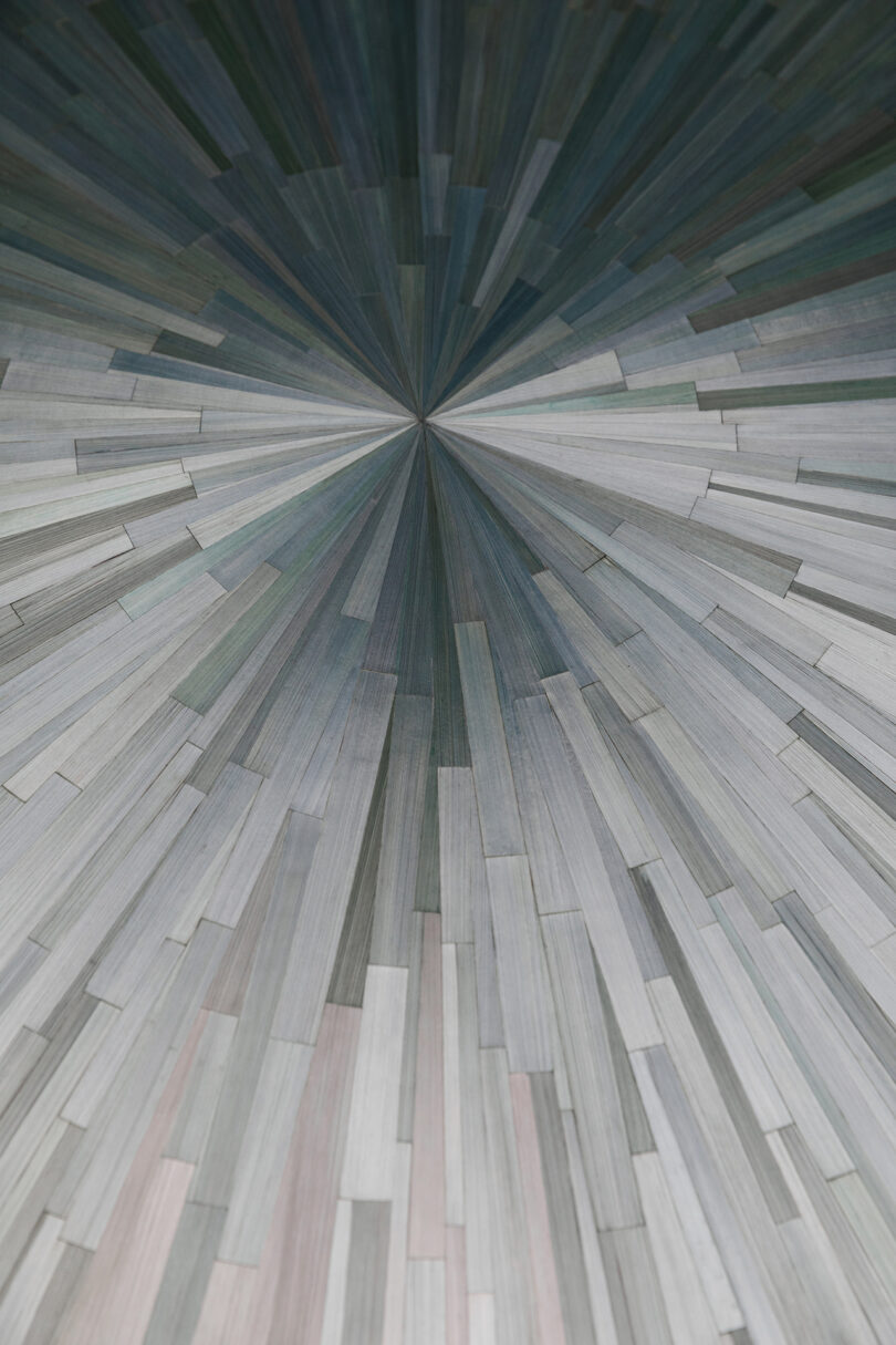 A geometric starburst pattern created with elongated straw tiles in muted gray and blue tones.