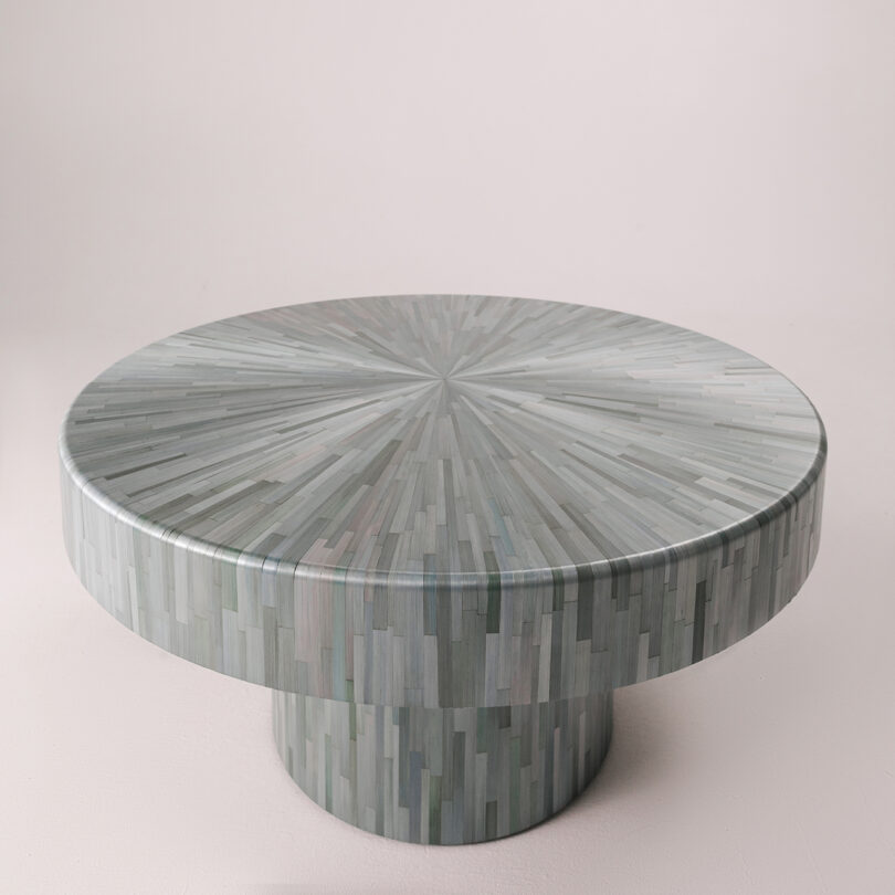 A modern coffee table with a glossy finish over a mosaic straw inlay in various shades of gray.