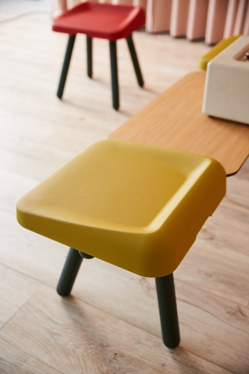 A mustard yellow Boln Slim stool with black legs in a bright, minimalist room with natural lighting.