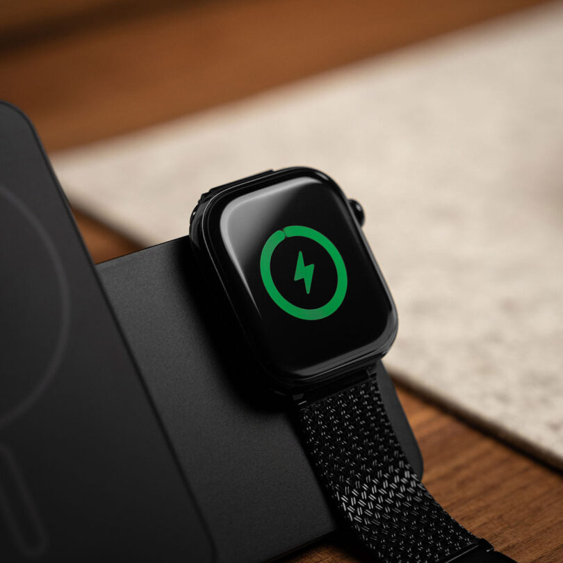 An Apple Watch resting on the Kuxiu charger's dedicated magnetic puck, showing the green charging status.