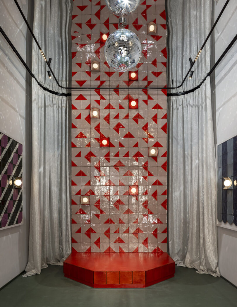 A small red stage with disco balls and silver curtains against a background of red and white diamond-patterned tiles.
