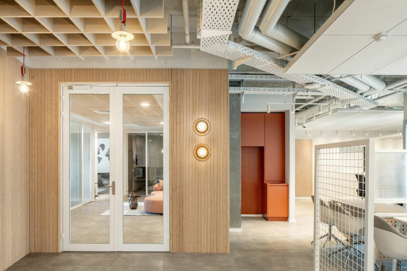 Office interior featuring wood-paneled walls, exposed ceiling pipes, and glass doors.