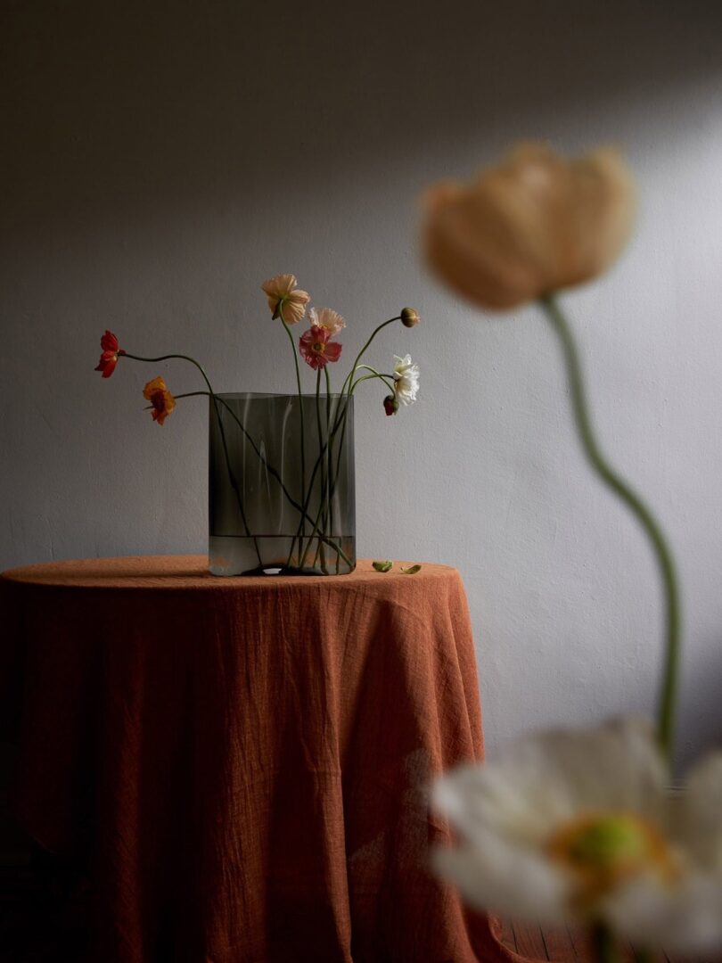 A bouquet of flowers in a minimalist vase sitting on a clothed table.
