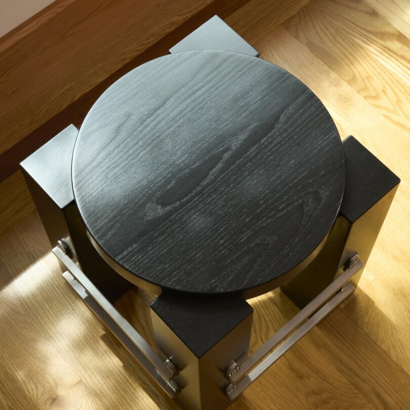 A round black wooden stool with square legs and industrial metal supports.