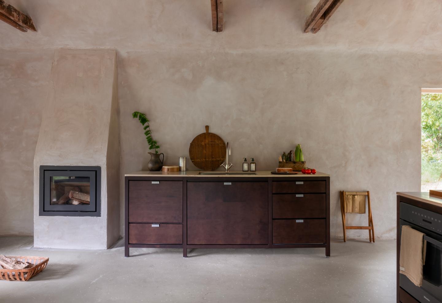 Luxury rustic modern kitchen featuring dark wood cabinetry and a stone fireplace against textured walls.
