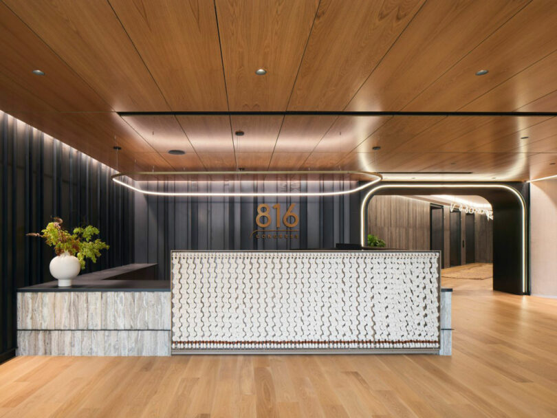 Detail of a textured stone reception desk with a white vase and '816' signage against a black wall.
