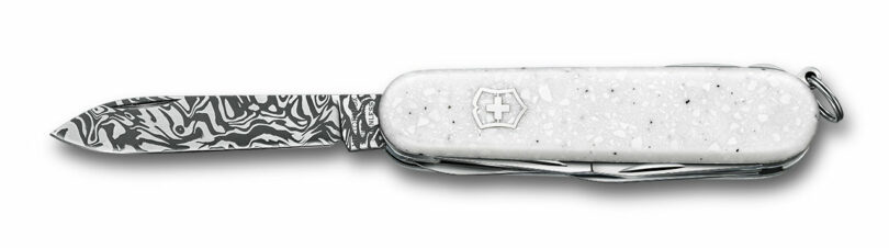 A Victorinox Swiss Army knife with a white handle and a Svavner-patterned Damasteel blade extended.