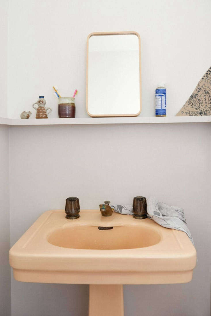 Minimalist powder room with a vintage peach pedestal sink against a neutral background.