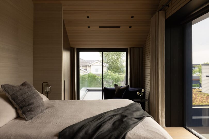 Modern bedroom with warm wood-paneled walls and a large sliding glass door overlooking greenery.