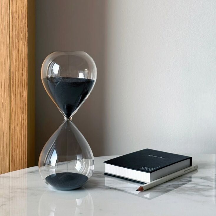 A black framed 30-minute desktop hourglass on a flat surface.