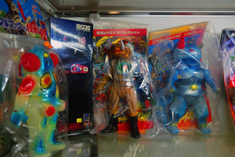 Three vintage Japanese action figures in plastic bags displayed on a shelf.