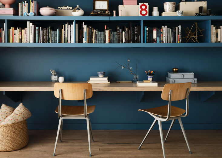 Home office with deep blue walls, a wooden floating desk, and built-in bookshelves.