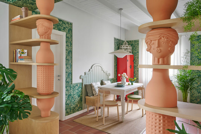 Dining area with whimsical terracotta sculpture shelving and green floral wallpaper.